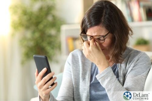 An image of a woman holding her cellphone while pinching her nose due to a headache