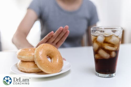 An image of a glass of soda and donuts with a woman waving her hand at the back