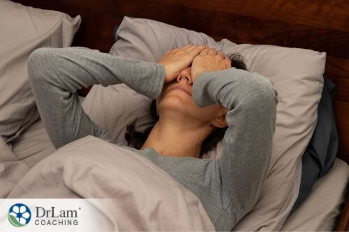 An image of a woman in bed while holding her eyes with both hands
