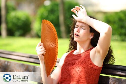 An image of a woman wiping her forehead while using a fan